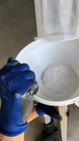 Operario con guantes vierte un material en polvo mediante un embudo en el interior de un tubo metálico rectangular.