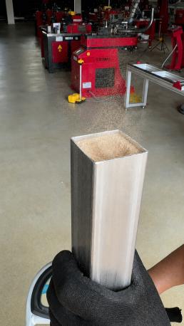 Operario sostiene un tubo metálico rectangular relleno hasta el borde con colofonia solidificada antes del proceso de curvado.